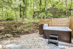 Un bain à remous situé dans un espace boisé, avec une terrasse en bois et des marches menant à celui-ci.
