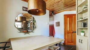 A kitchen with a wooden table, a hanging copper light fixture, a round mirror, and a wooden door. - Mountain Retreat: Year-Round Getaway, Pup Friendly (Wintergreen Resort)