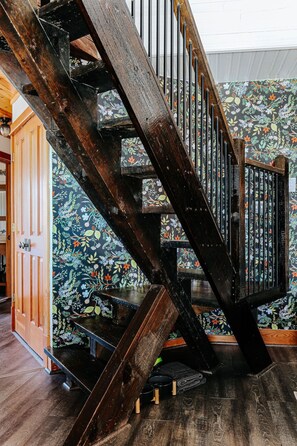 Un escalier en bois sur fond d’un papier peint à motifs floraux.