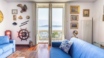 Une pièce avec un canapé bleu, un plancher en bois, un élément décoratif en forme de roue de navire et une vue sur la mer par une grande fenêtre.