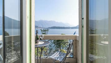 Un balcon avec une table, une chaise et un verre à vin, donnant sur un lac et des montagnes.
