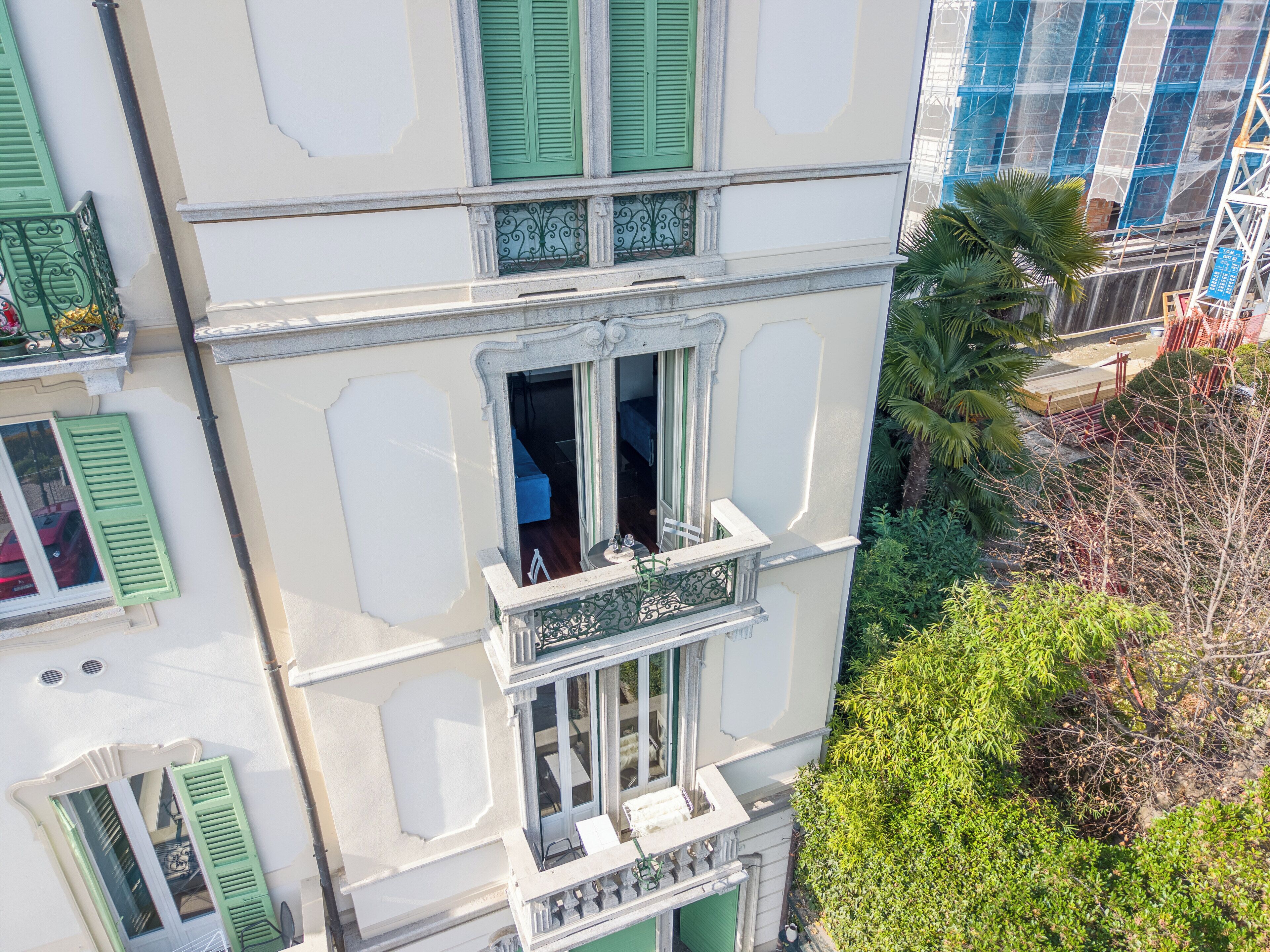 Un edificio a più piani con persiane verdi, un balcone con ringhiere decorate e vista su un cantiere edile.