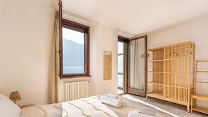 Quarto com cama, guarda-roupa de madeira, janela com vista e radiador.