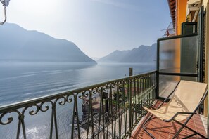 Een balkon met een stoel, een leuning en uitzicht op een rustig waterlichaam met bergen op de achtergrond.