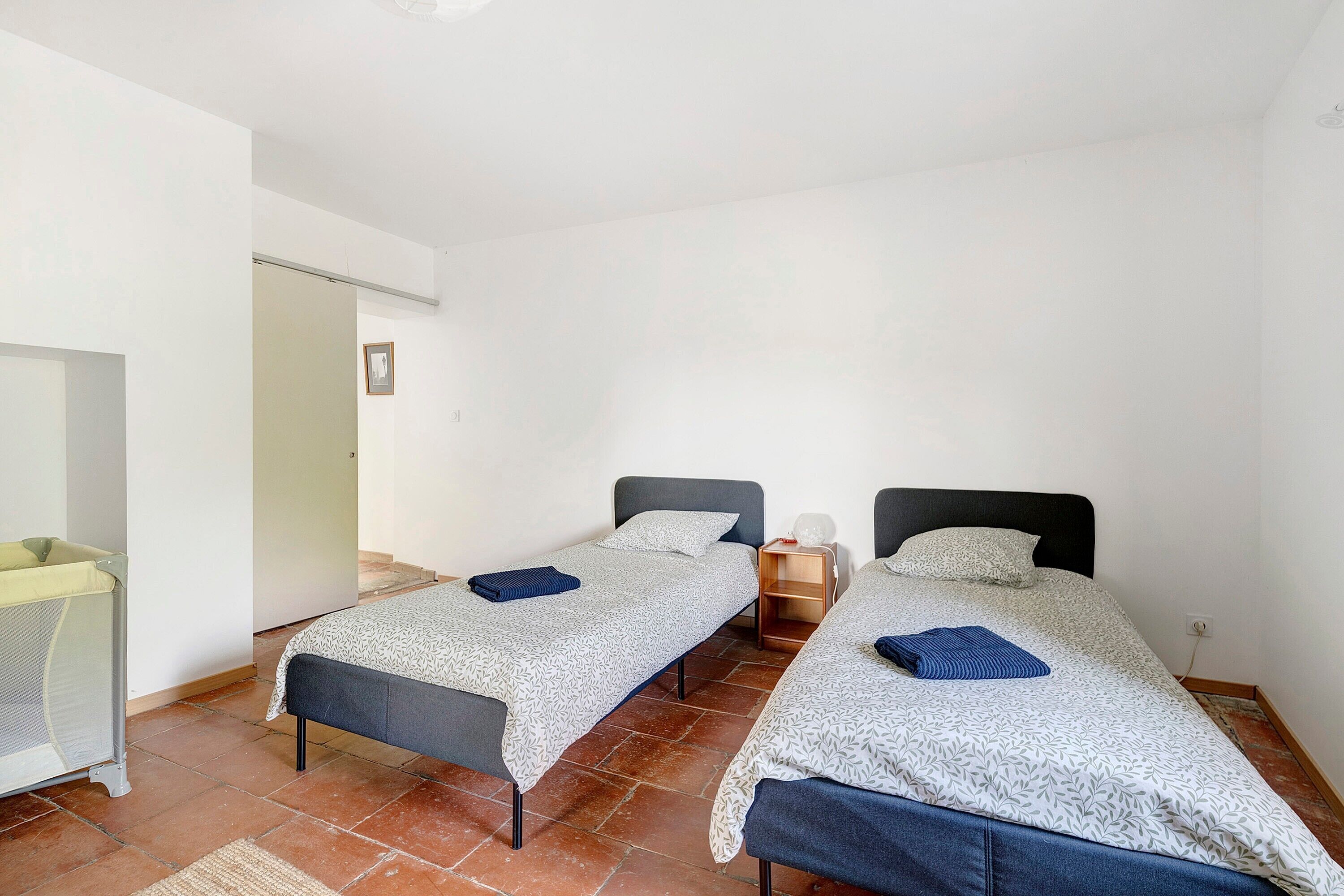 A room with two beds, a small table, a chair, and a door.