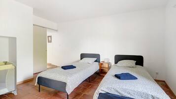 A room with two beds, a small table, a chair, and a door.