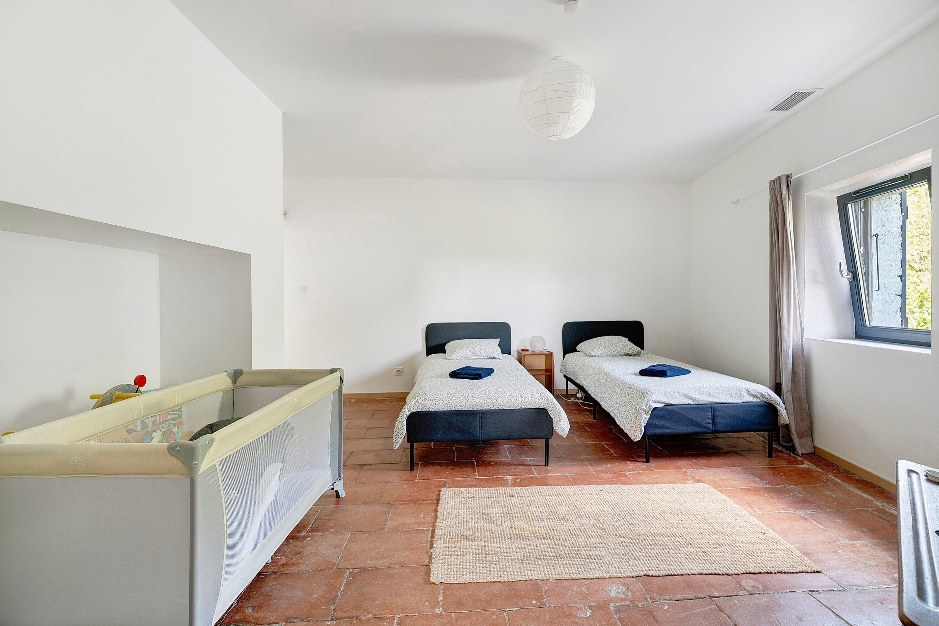 Ein Zimmer mit zwei Betten, einem Babybett, einem Fenster mit Vorhängen und einer Heizung.