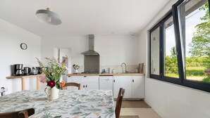 Une cuisine moderne avec des armoires blanches, une hotte en acier inoxydable et un coin repas avec une table dressée pour deux personnes.