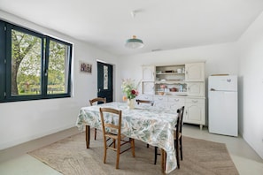 A dining area with a table, chairs, a rug, a window, and a kitchen area with cabinets and a refrigerator.