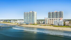 A coastal hotel with multiple floors, a beach view, and a pier extending into the water. - Prince Resort 1904- Oceanfront 2 Bedroom-Pool (North Myrtle Beach)