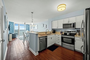 A modern kitchen with white cabinets, stainless steel appliances, and a wooden floor. - Prince Resort 1904- Oceanfront 2 Bedroom-Pool (North Myrtle Beach)