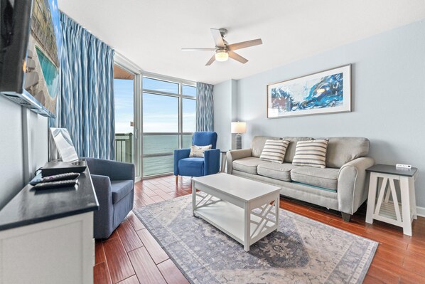 A living room with a sofa, armchair, coffee table, and a painting on the wall. - Prince Resort 1904- Oceanfront 2 Bedroom-Pool (North Myrtle Beach)