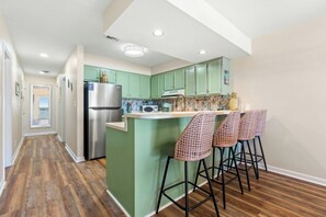 A kitchen with green cabinets, a stainless steel refrigerator, and a bar area with wicker chairs. - Coastal Shores B3- Amazing Oceanfront 2 Bedroom (North Myrtle Beach)