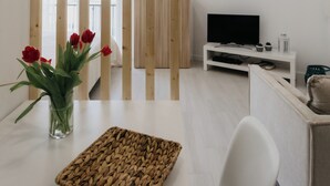 Een moderne woonkamer met een televisie, witte meubels, een geweven mand en rode bloemen op een tafel.