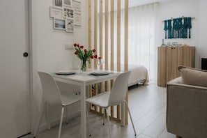 Un comedor moderno con una mesa blanca, dos sillas, un jarrón de flores rojas y un separador de madera.