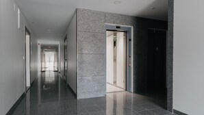 Een moderne hal met gepolijst stenen vloerwerk, een glazen lift en een deur die naar een kamer leidt.