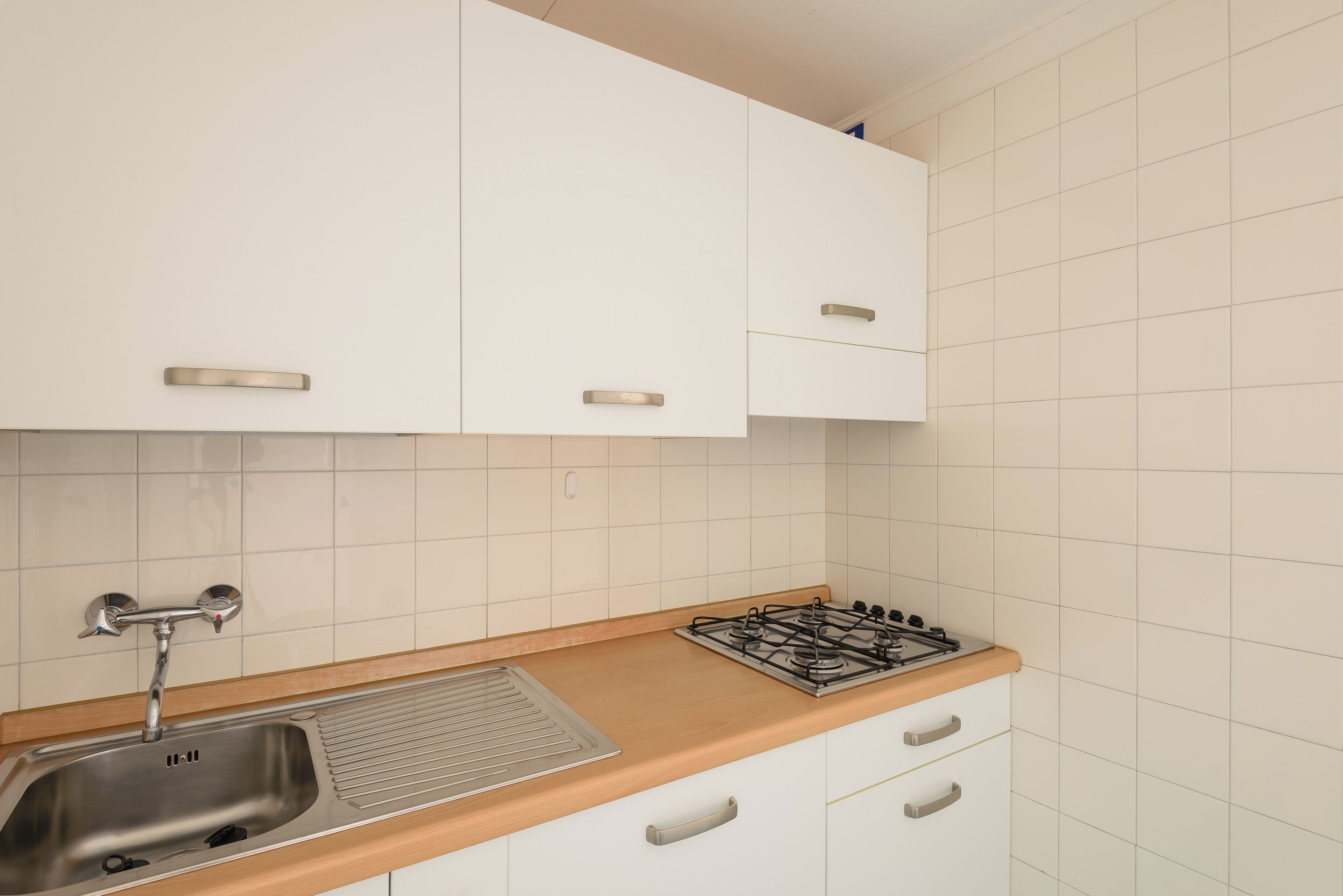 A kitchen with white cabinets, a stainless steel sink, a wooden countertop, and a gas stove.