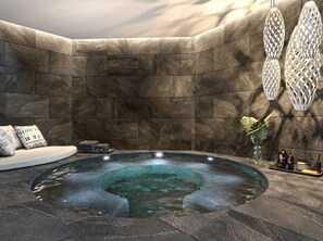 Ein Wellnessbereich mit Whirlpool, Steinwänden und einer Sitzecke mit Kissen.