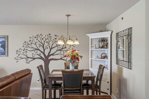 A dining area with a tree decal, a chandelier, a flower vase, and a white cabinet with decorative items. - Waterfront Osage Beach Condo w/ Boat Slip & Pool Access (Osage Beach)
