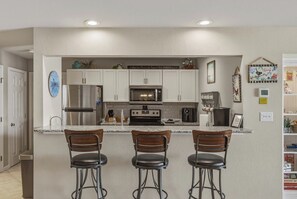 A kitchen with white cabinets, stainless steel appliances, a marble countertop, and three bar stools. - Waterfront Osage Beach Condo w/ Boat Slip & Pool Access (Osage Beach)