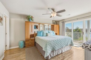 Een slaapkamer met een bed, een houten garderobe, een plafondventilator en uitzicht op het omliggende landschap.