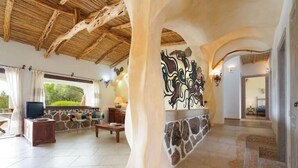 A spacious living area with a stone fireplace, a television, and a large window with curtains. - Villa Giulia: a charming retreat among the rocks of the Costa Smeralda (Arzachena)