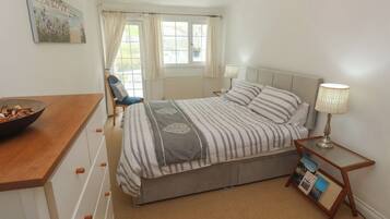 A bedroom with a bed, a chair, a bedside table with a lamp, a window with curtains, and a painting on the wall.