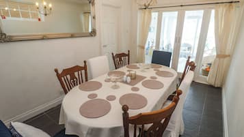 Un comedor con una mesa redonda, sillas, una araña, un espejo y vistas a través de un puerta de cristal.