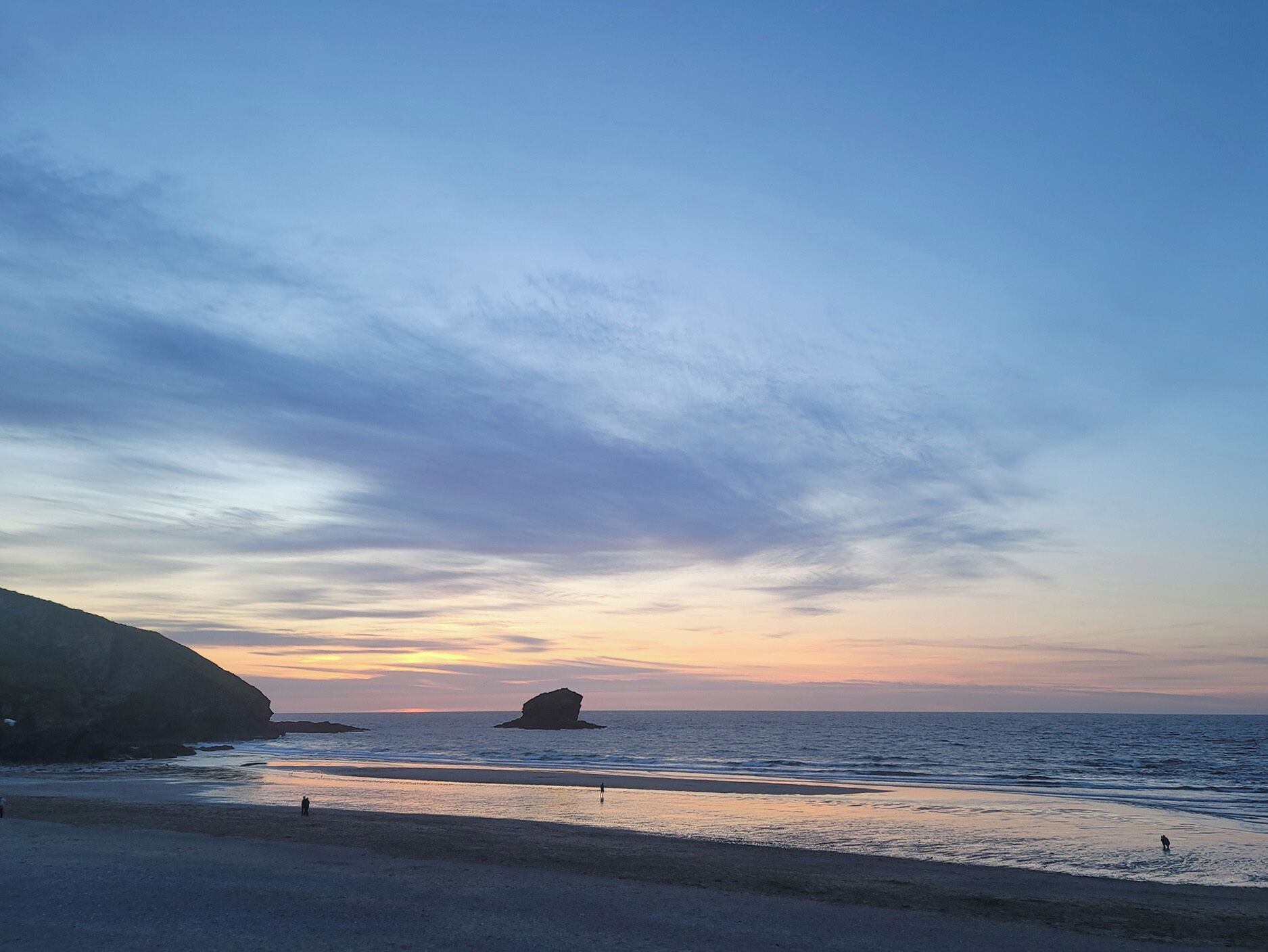 A beach with a rocky outcrop and calm sea under a clear sky.