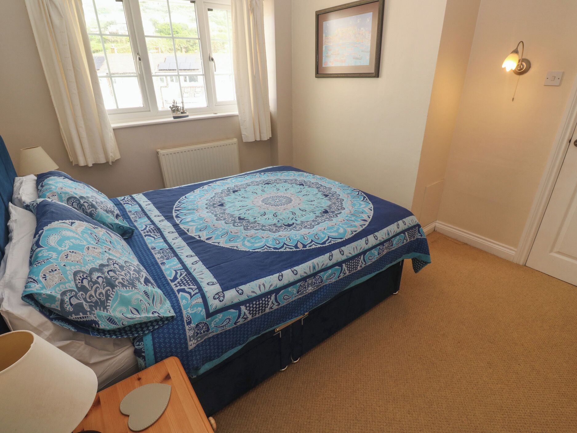 A bedroom with a bed, a window, a radiator, a framed picture, and a wall-mounted light fixture.
