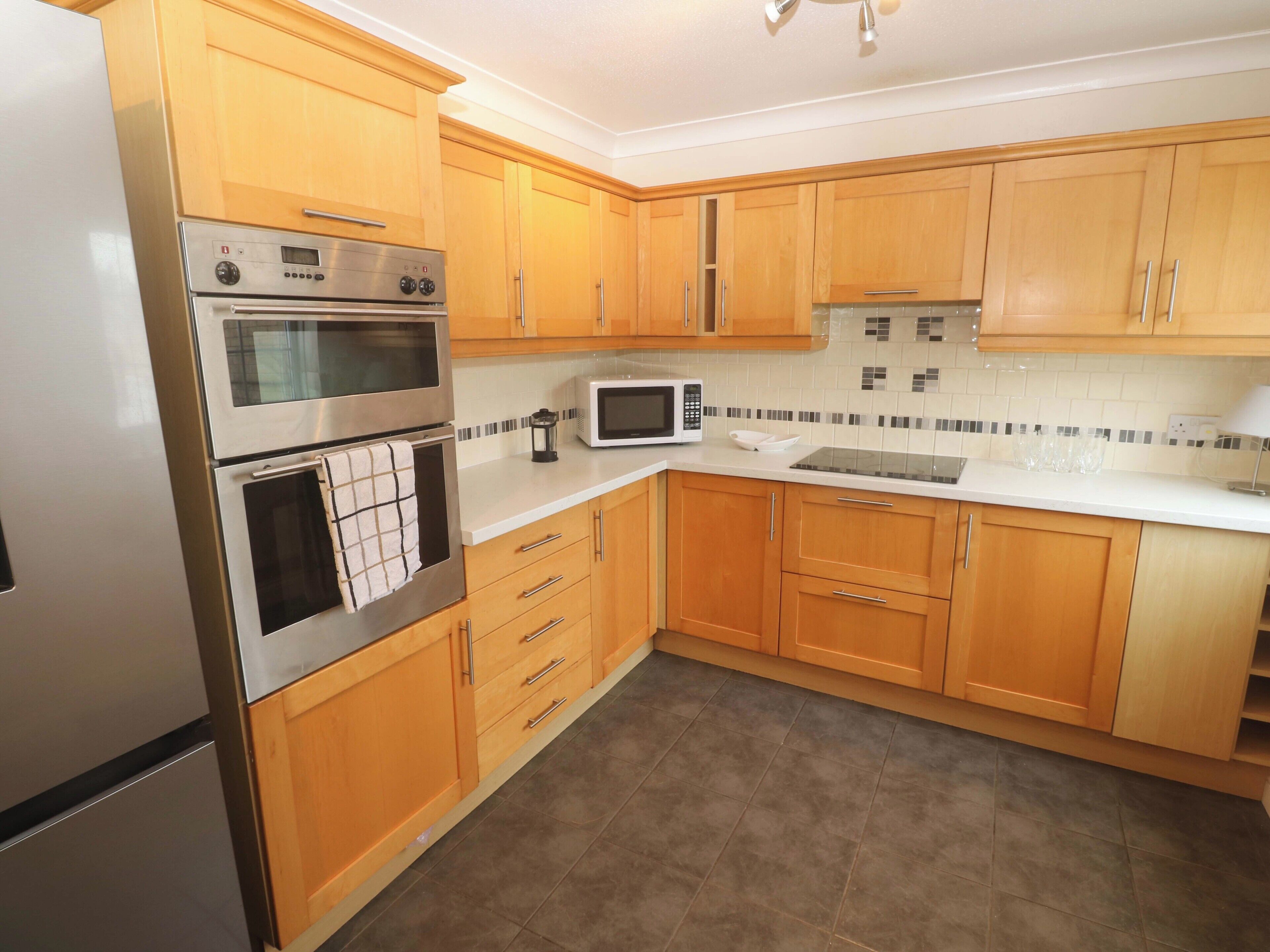 A kitchen with wooden cabinets, a stainless steel oven, a microwave, and a tiled backsplash.