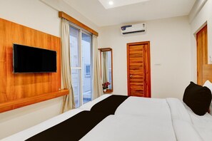 Habitación de hotel con cama, televisor montado, ventana con cortinas, puerta y unidad de aire acondicionado.