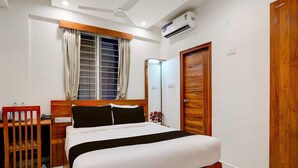 A hotel room with a bed, bedside table, desk, chair, window with curtains, mirror, wardrobe, and ceiling fan. - Classic With Balconyroyal Avenue (Bengaluru)