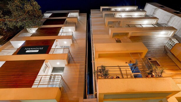 A multi-story building with a modern architectural design, featuring a central staircase, balconies, and a sign that reads 'TOWNHOUSE & Company Services.' - Classic With Balconyroyal Avenue (Bengaluru)