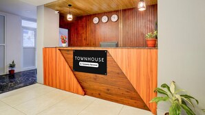 A reception desk with a wooden finish, a sign indicating 'Townhouse Company-Serviced,' and a potted plant on the right. - Classic With Balconyroyal Avenue (Bengaluru)