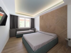 Ein modernes Schlafzimmer mit einem großen Bett, einem kleineren Bett, einem an der Wand befestigten Fernseher und einem Fenster mit Vorhängen.