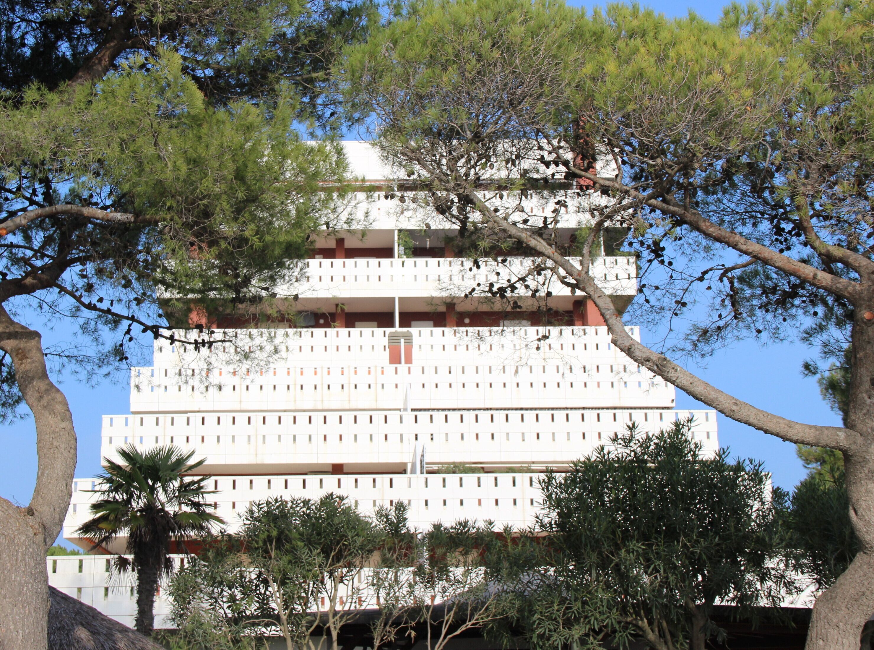 Un immeuble à plusieurs étages, doté d’une façade blanche, de balcons et entouré d’arbres.