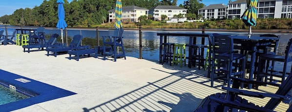 A waterfront deck with lounge chairs and umbrellas, a pool, and residential buildings in the background. - Waterway front 2-BR 2 bath condo Boat Ramp & Dock Tennis, Pool Myrtle Beach (Myrtle Beach)