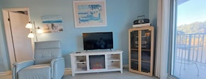 A living room with a TV, a fireplace, a chair, and a balcony with outdoor furniture. - Waterway front 2-BR 2 bath condo Boat Ramp & Dock Tennis, Pool Myrtle Beach (Myrtle Beach)