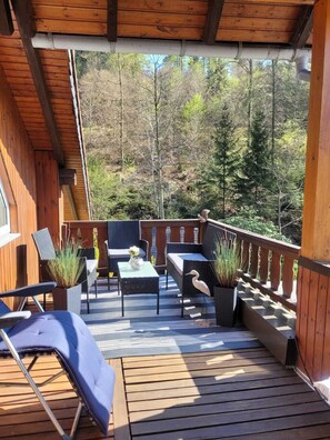 A wooden deck with outdoor furniture, including chairs and a table, surrounded by potted plants. - Oasis Eichelbachtal (Bad Grund (Harz))