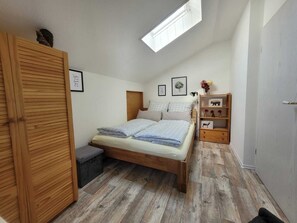 A bedroom with a wooden bed, a skylight, a bedside shelf with decorative items, and a wardrobe. - Oasis Eichelbachtal (Bad Grund (Harz))