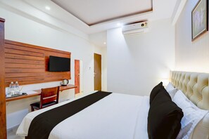 A hotel room with a bed, a desk, a chair, a television, and a wall-mounted air conditioning unit. - Premium Palette Hotel and Resort (Bengaluru)
