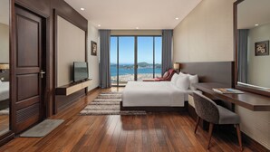A hotel room with a large bed, a desk, a chair, a TV, and a view of the sea. - Villa Nha Trang Ocean Front Luxury Abogo (Nam Nha Trang)