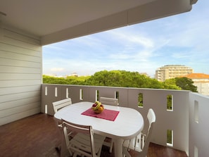 Ein Balkon mit weißem Tisch und Stühlen, einer Obstschale und Blick auf Gebäude und Bäume.