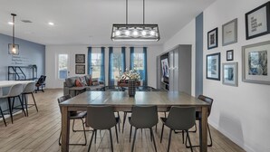 Un comedor moderno con una mesa de madera, cuatro sillas, un florero con flores, un sofá y una cocina al fondo.