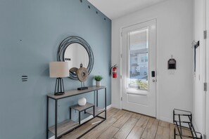 Ein Flur mit blauer Wand, einem runden Spiegel, einem Konsolentisch mit Lampe, einer kleinen Pflanze und einem Feuerlöscher.