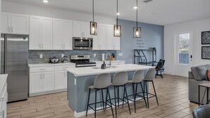 Una cocina moderna con armarios blancos, electrodomésticos de acero inoxidable y una isla central con taburetes de bar.