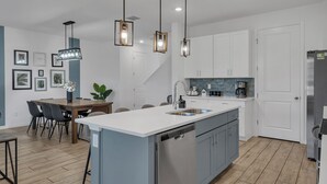 Una cocina moderna con una isla central, electrodomésticos de acero inoxidable e iluminación colgante.