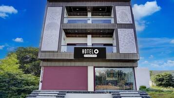 A modern hotel with a sign reading 'HOTEL O Company-Serviced,' a balcony on the second floor, and a red garage door.