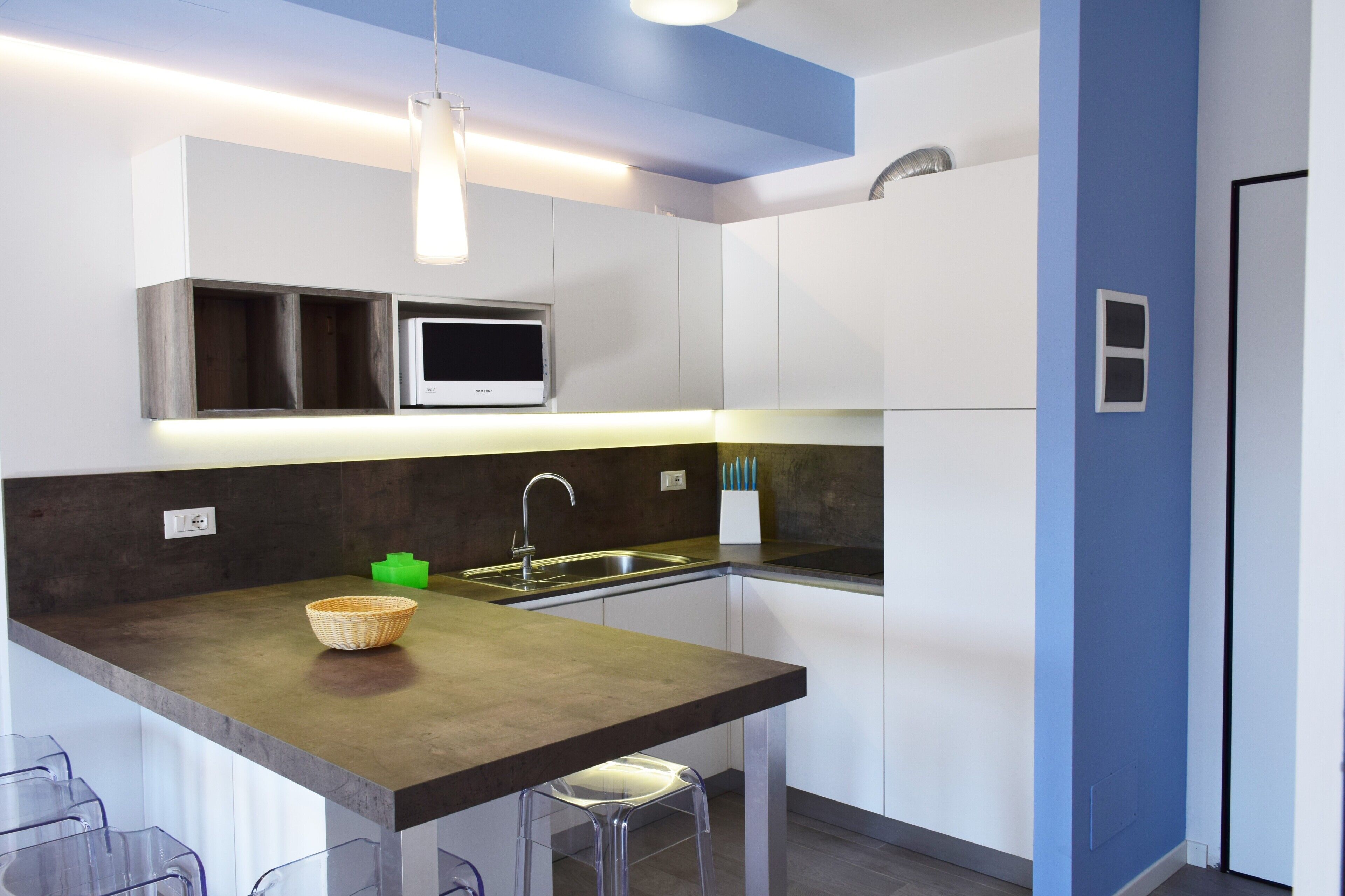 A modern kitchen with a dark countertop, white cabinets, a built-in microwave, and a stainless steel sink.